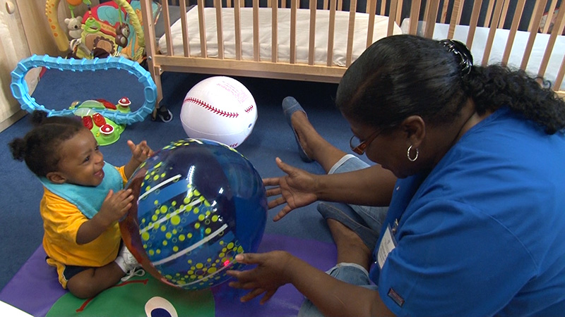 A staff member plays with a toddler with an inflatable beach ball