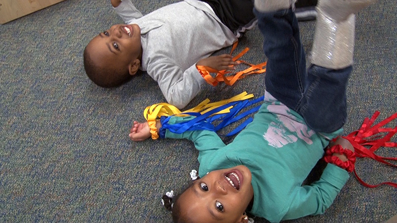 Two toddlers lay on the floor with ribbons