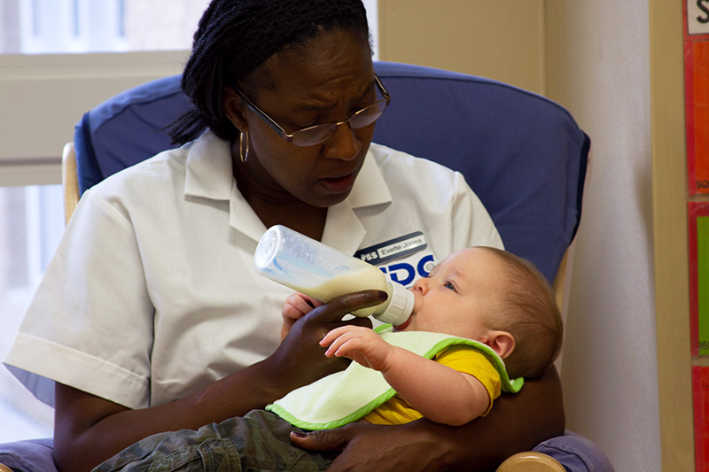 A caregiver bottle feeds an infant