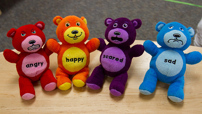 Four stuffed bear toys each have a different emotion printed on the belly and have corresponding facial expressions