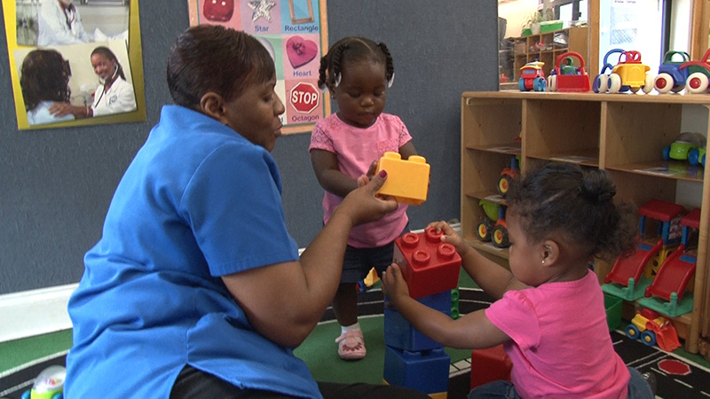 A caregiver plays with a couple toddlers with connecting building block toys