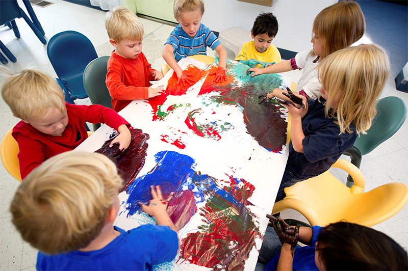 toddlers and their care-giver finger-paint at a round table