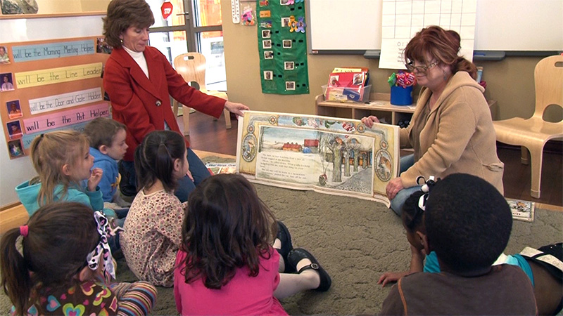 Care-givers show the page of a book to children during story-time