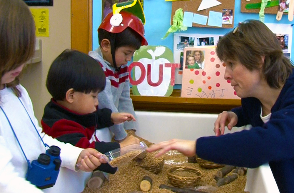 Children learn with their caregiver while using a sensory table