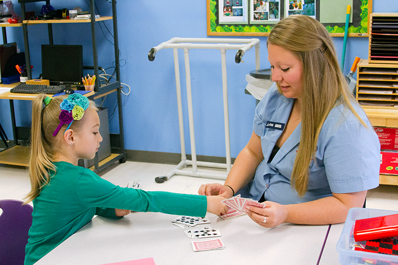 A caregiver plays cards with a child at a table
