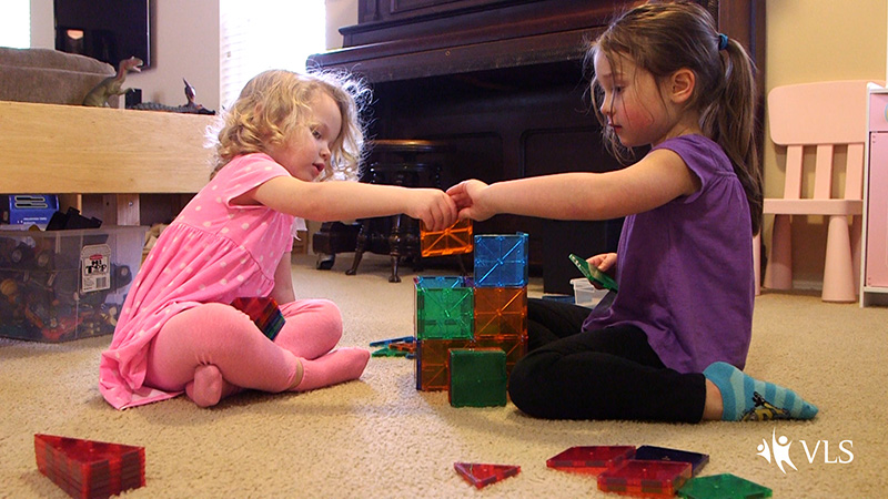 two preschool age children work together to build a structure with magnetic colored blocks