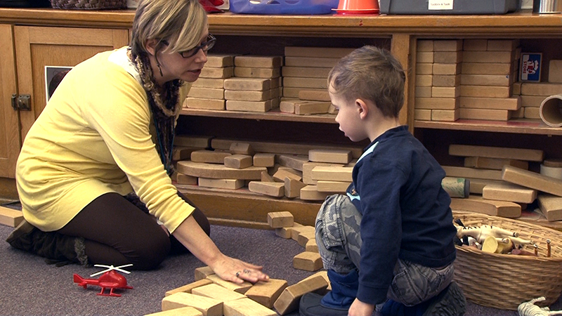 Teacher instructing preschool child about the proper usage of wooden blocks