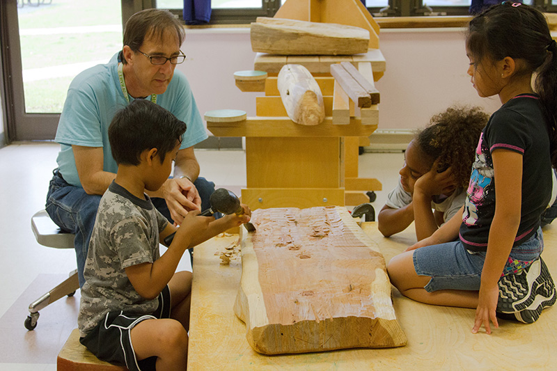 Children chisel a block of wood under their caregiver's supervision